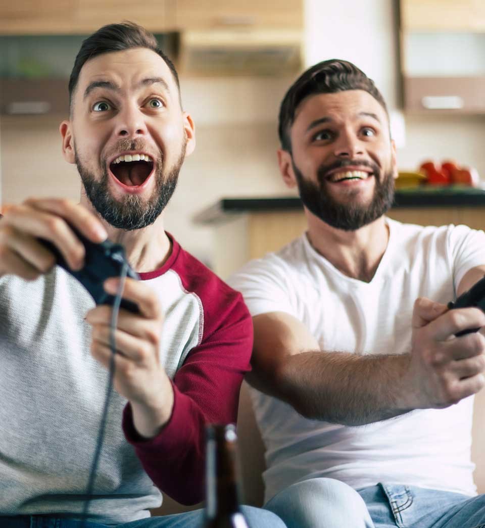 Excited smiling men playing in video games on tv at home on the couch. Friends with joysticks play game with happy emotions on faces