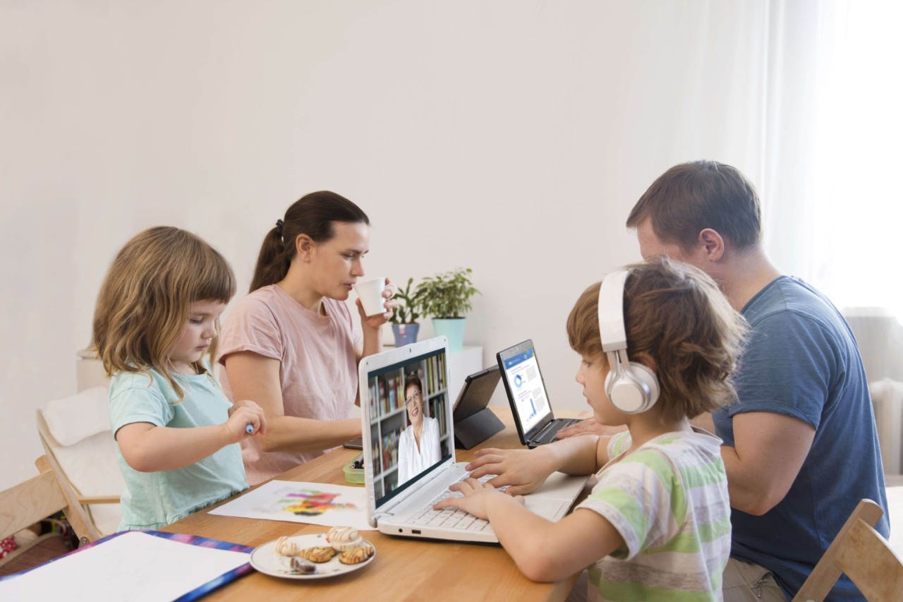 family Mom, dad and two  kids Sitting at the table all together. Children learn onlay from home. work from home with kids. quarantin. Home office.