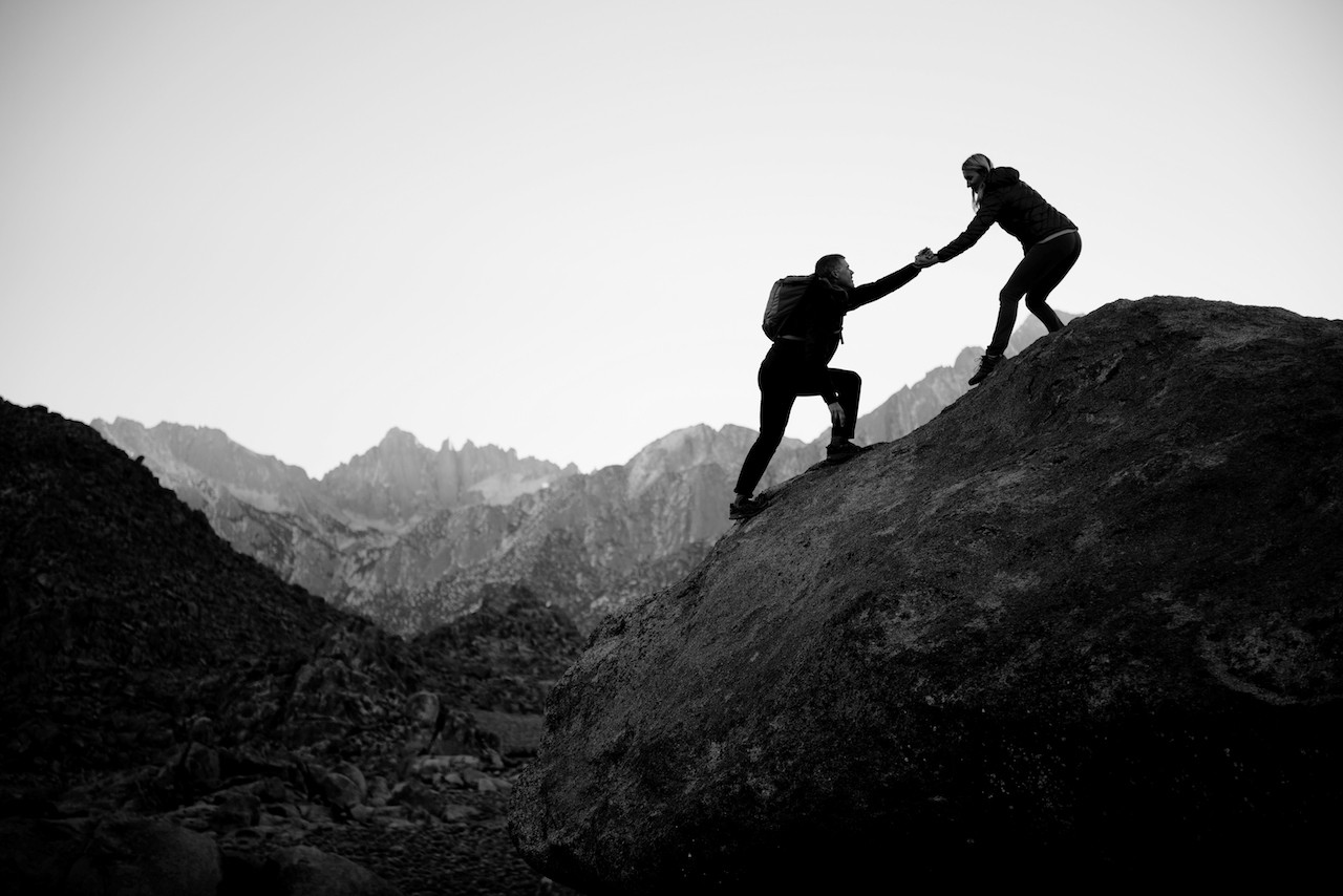 Two hikers climbing a mountain and holding hands to depict Juniper Networks support services
