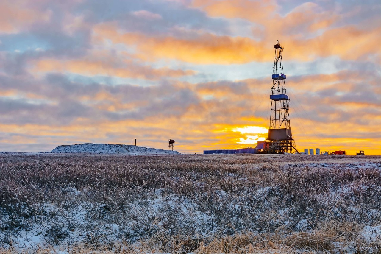Vegetation of the northern tundra in the winter in the Arctic. In the background is a drilling rig for oil and gas drilling. The sun of the polar day sparkles through the clouds. Backlighting.